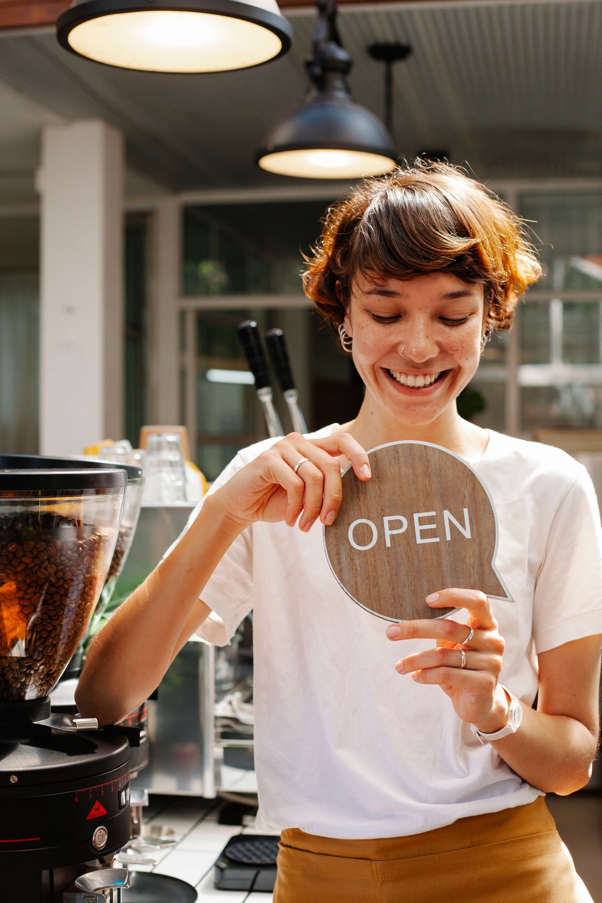 A smiling café owner holding an OPEN sign behind the counter