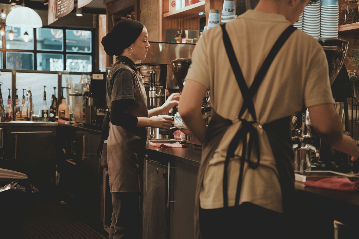 Two baristas making coffee behind a café counter