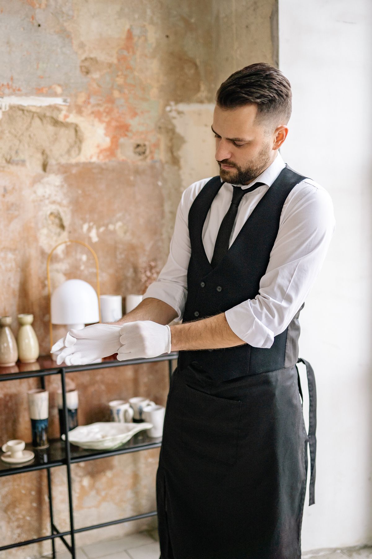 A waiter in a vest and gloves setting up for table service
